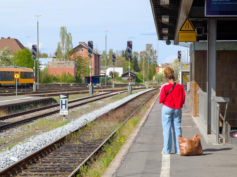 Eine Frau steht auf dem Bahnsteig und ihre Tasche steht auf den Boden, während sie am Bahnhof Weiden in Bayern auf einen Zug wartet. Eine Frau steht auf dem Bahnsteig und ihre Tasche steht auf den Boden, während sie am Bahnhof Weiden in Bayern auf einen Zug wartet.