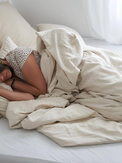 Eine junge Frau liegt mit geschlossenen Augen im Bett, es wird schon hell.