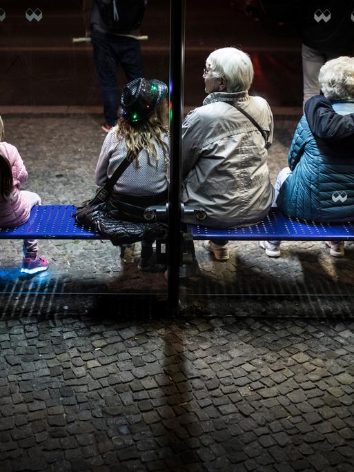 Junge und alte Menschen sitzen im Jahr 2018 auf der Bank einer Bushaltestelle in Berlin