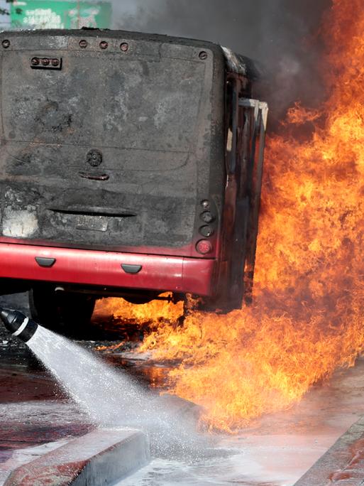 Einsatzkraft der Feuerwehr löscht auf einer Hauptstraße in Zapopan einen brennenden Bus (Mexiko, 22.02.2026)