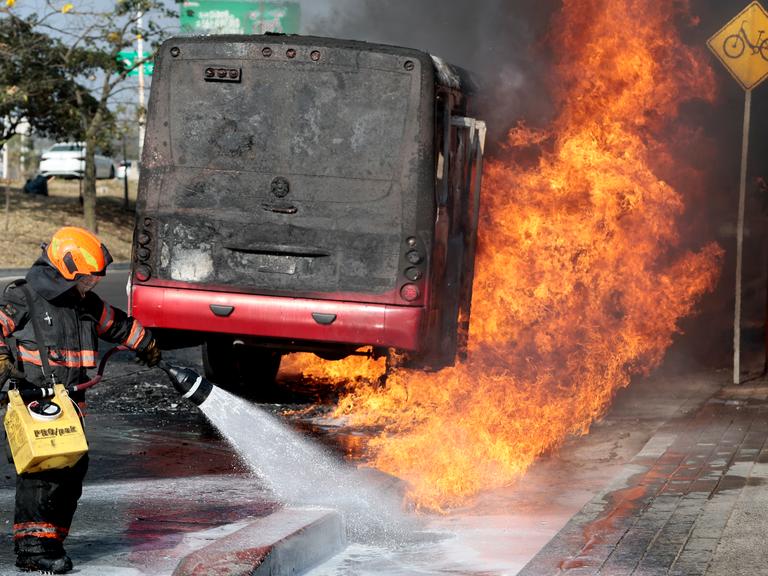 Einsatzkraft der Feuerwehr löscht auf einer Hauptstraße in Zapopan einen brennenden Bus (Mexiko, 22.02.2026)