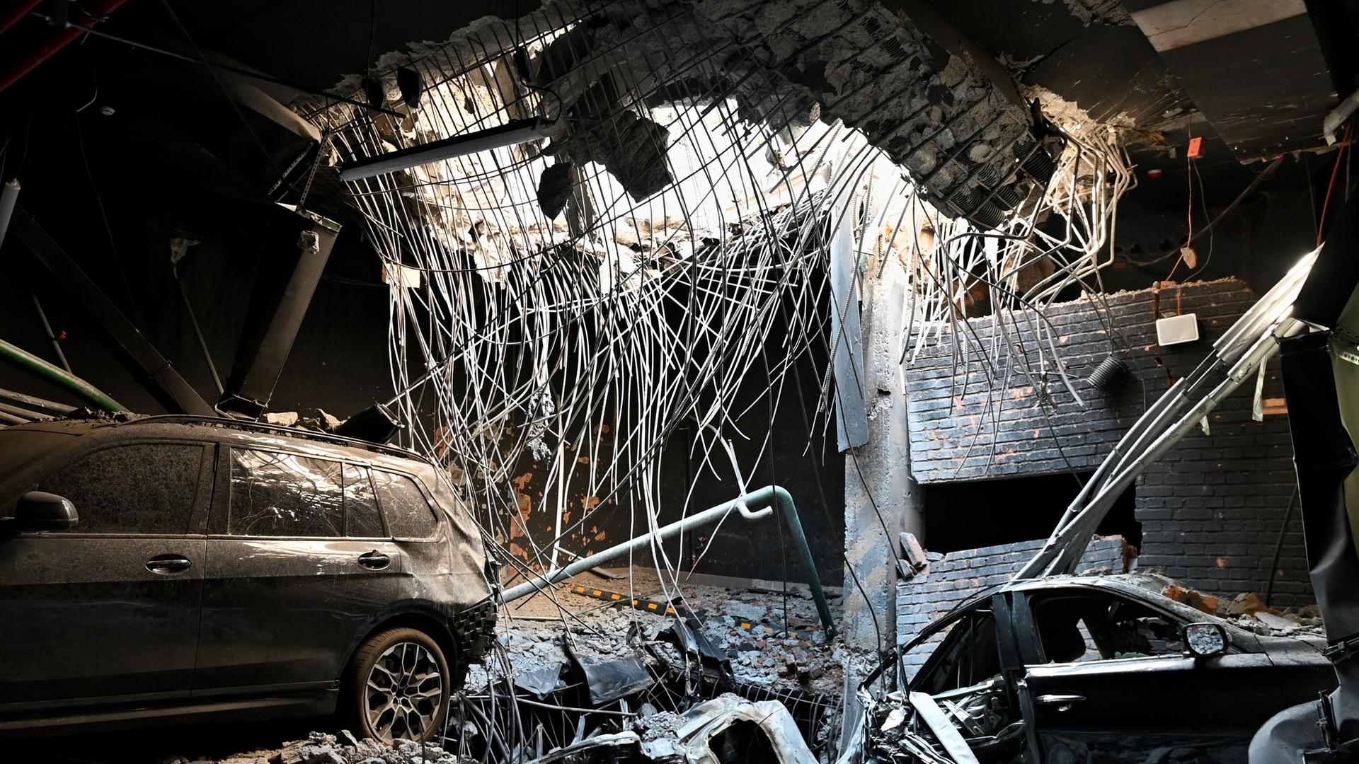 Kiew, Ukraine: Ein Loch in einer Geschossdecke durch eine Raketenexplosion und beschädigte Autos auf dem Parkplatz eines Wohngebäudes, das durch einen massiven russischen Raketenangriff beschädigt wurde.