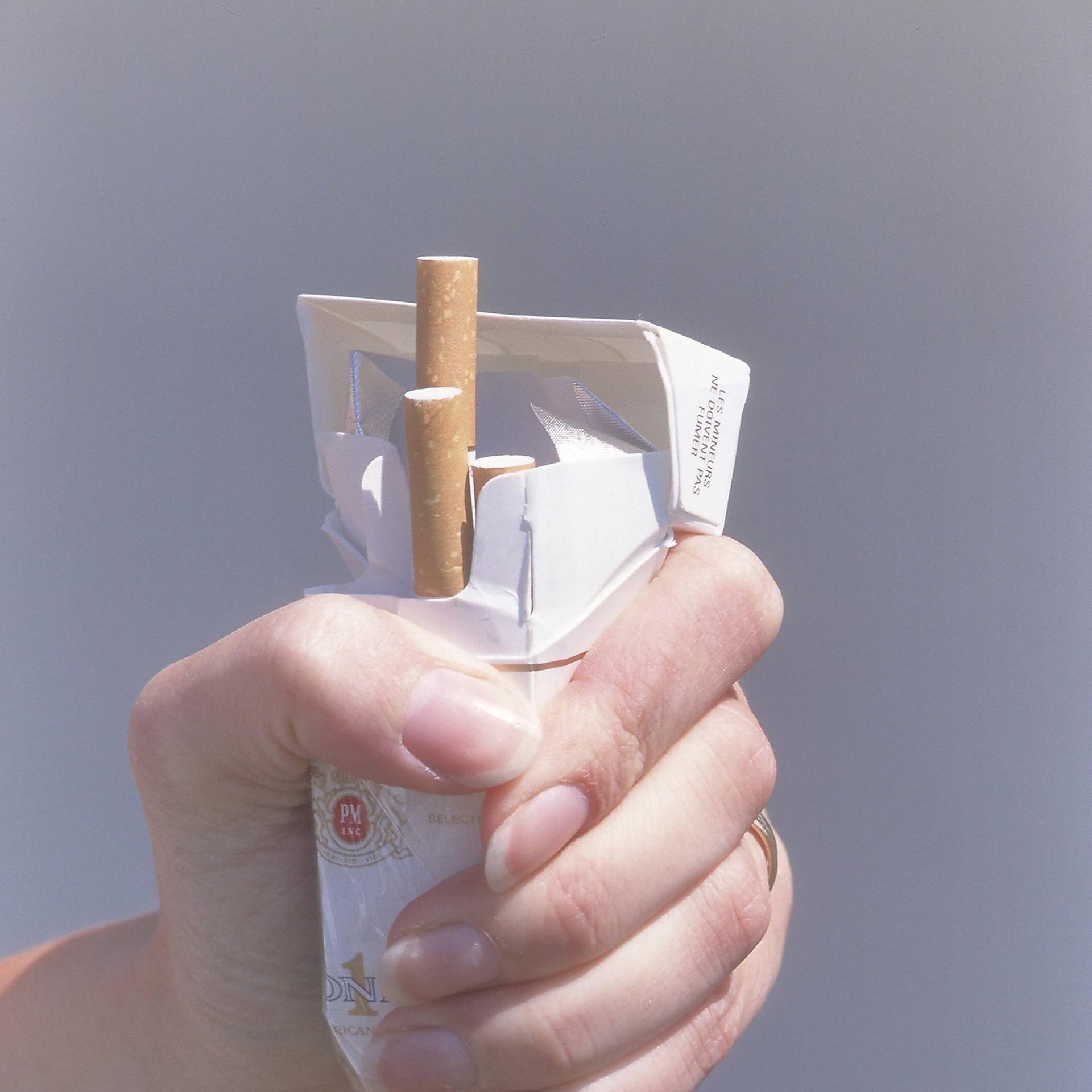 Eine Hand, die eine Packung Zigaretten zerquetscht.