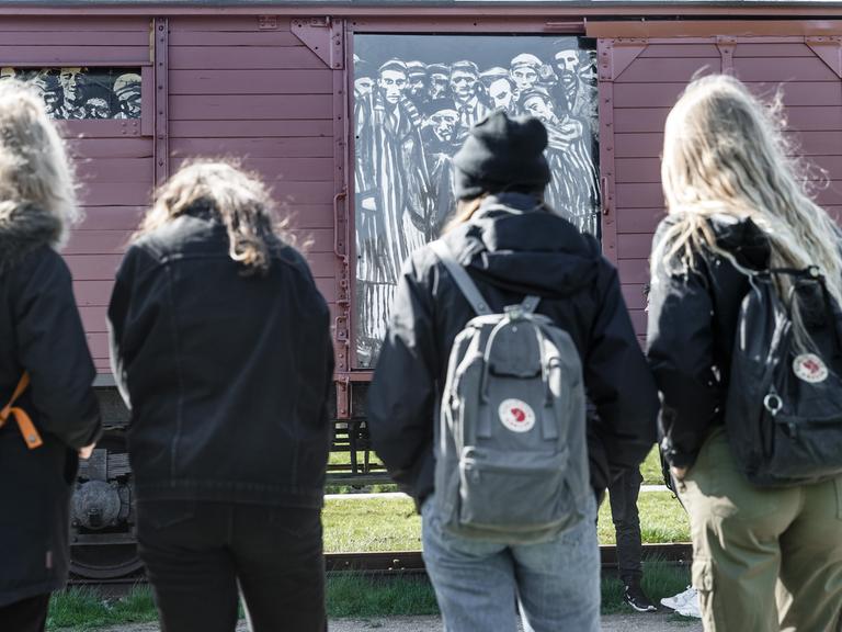 Schülerinnen betrachten einen historischen Reichsbahnwaggon im ehemaligen Lagerbahnhof des Konzentrationslagers Neuengamme steht