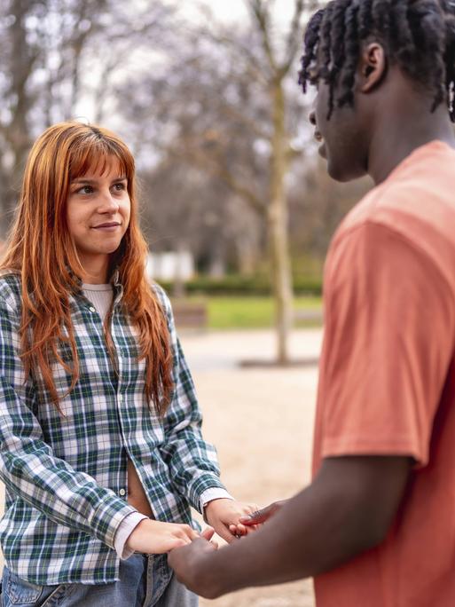 Eine junge Frau und ein junger Mann stehen sich gegenüber. Sie halten Händchen.