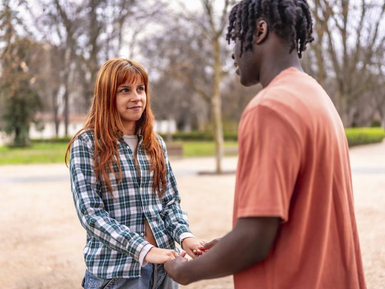 Eine junge Frau und ein junger Mann stehen sich gegenüber. Sie halten Händchen.