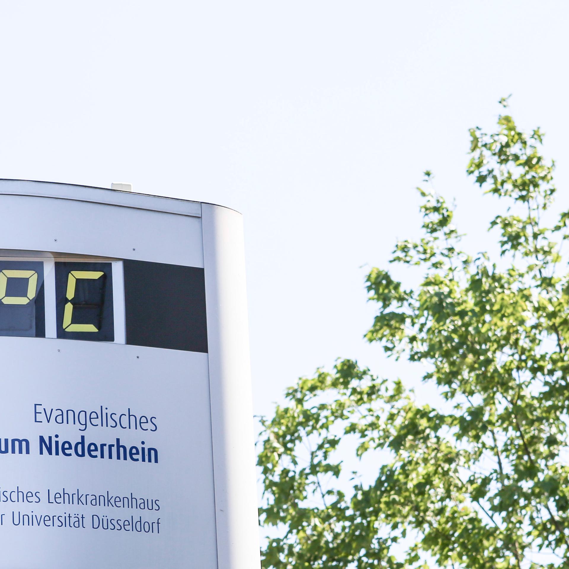 Thermometer vor Krankenhaus zeigt 39 Grad, daneben ein Baum