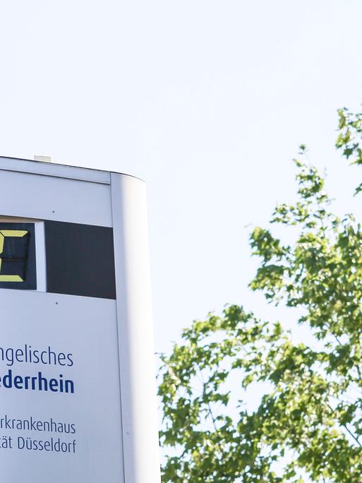 Thermometer vor Krankenhaus zeigt 39 Grad, daneben ein Baum