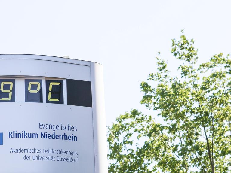 Thermometer vor Krankenhaus zeigt 39 Grad, daneben ein Baum