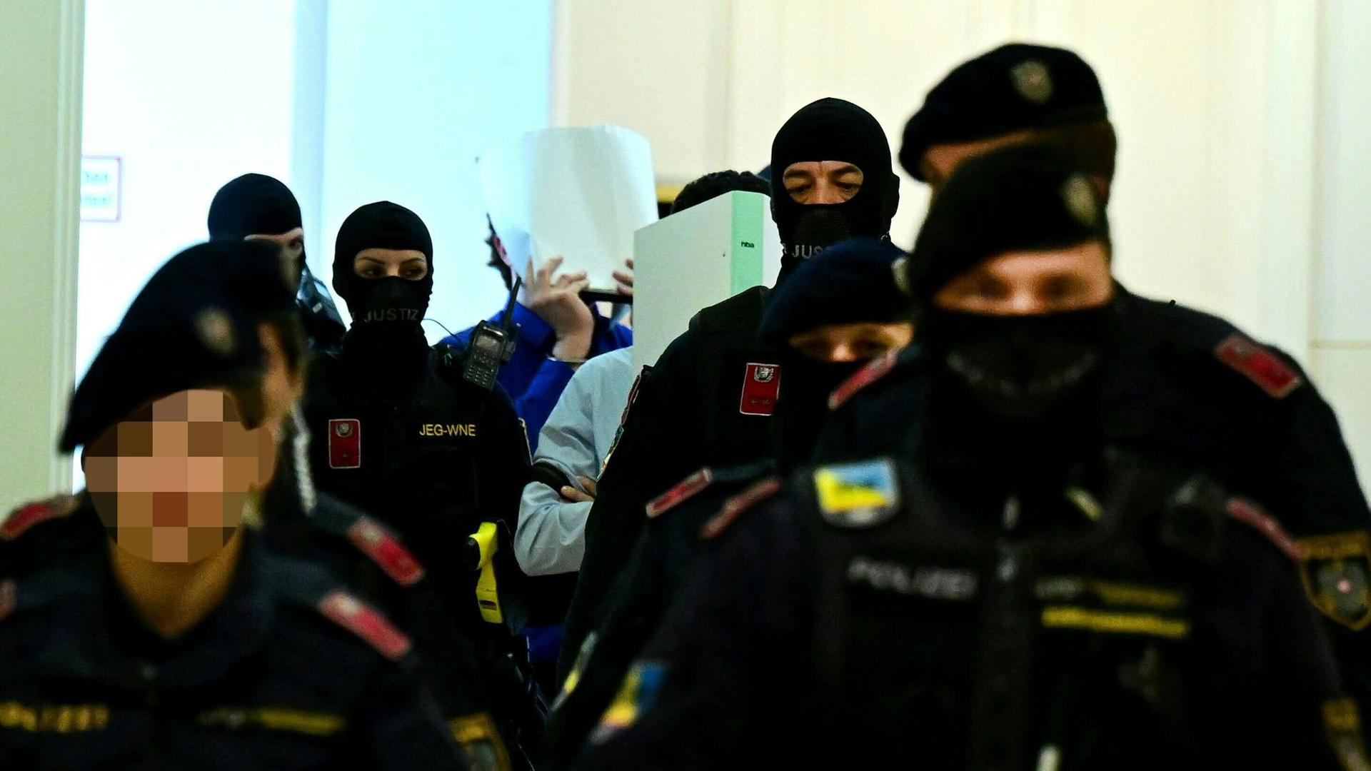Die Angeklagten vor Verhandlungsbeginn am Landesgericht Wiener Neustadt. Sie halten ihre Gesichter bedeckt und sind von vermummten Polizisten umgeben. Die Angeklagten vor Verhandlungsbeginn am Landesgericht Wiener Neustadt. Sie halten ihre Gesichter bedeckt und sind von vermummten Polizisten umgeben.