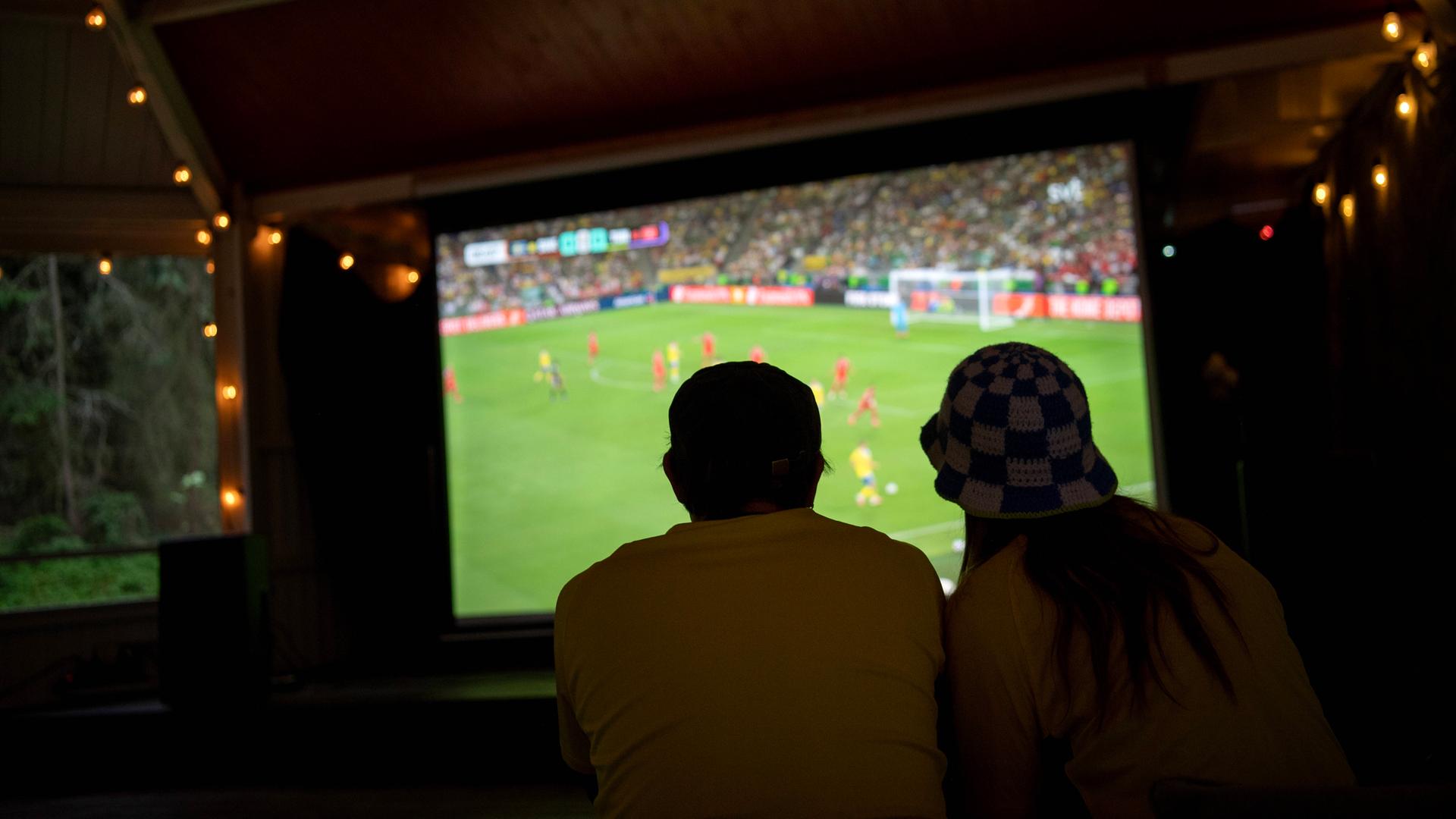 Fußballfans schauen ein Spiel der Weltmeisterschaft auf einem großen Bildschirm.