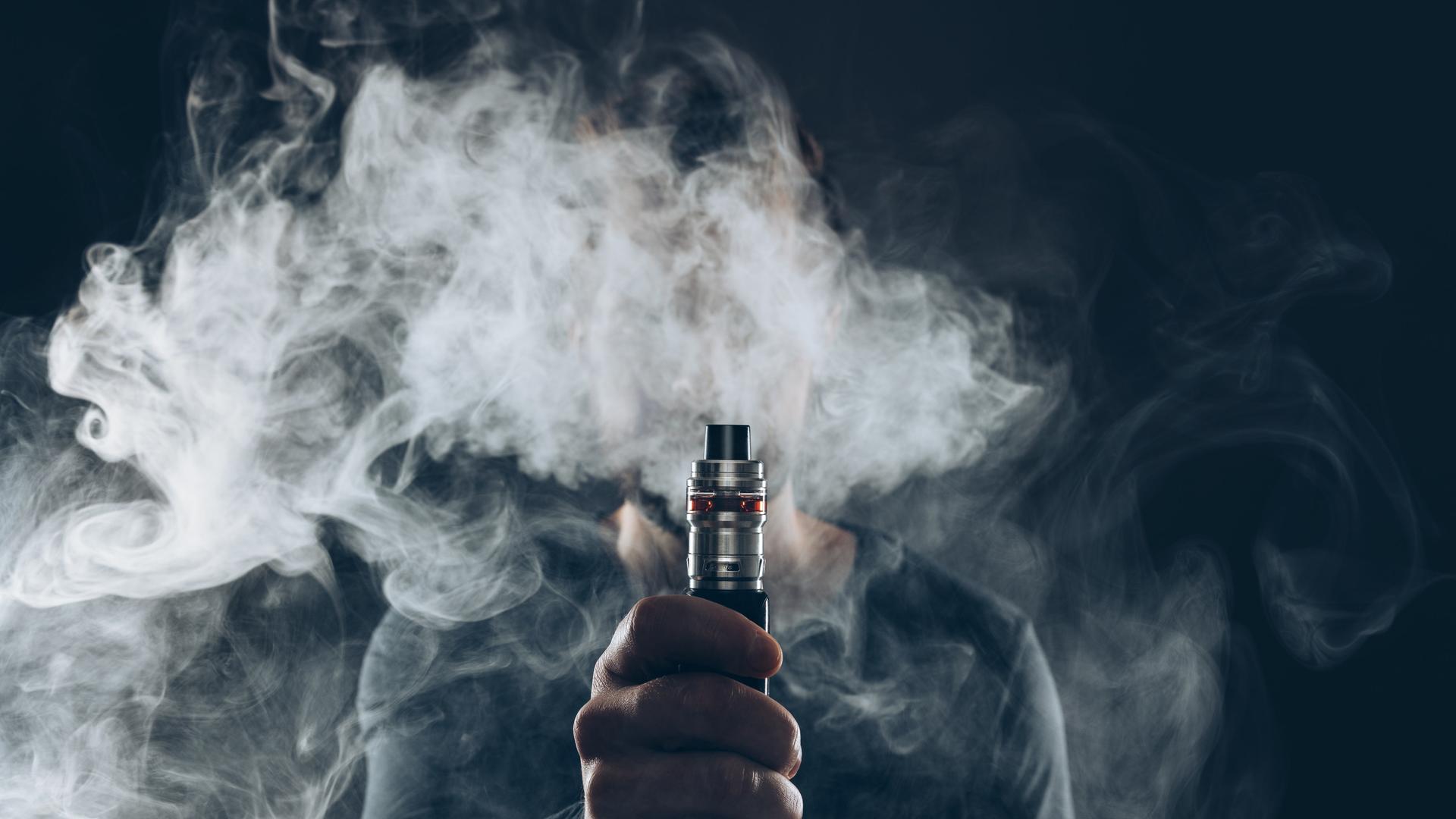 Ein Mann hält einen Vape hoch, der qualmt.