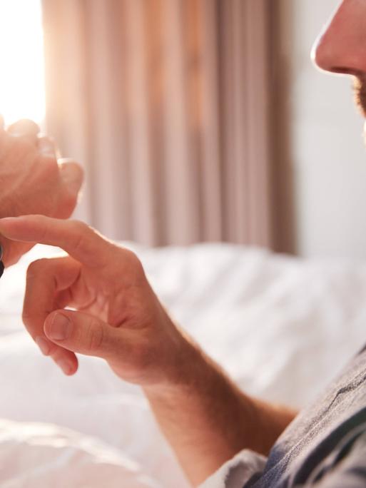 Ein Mann chekct den Verlauf seines Schlafs auf einem Fitnesstracker am Handgelenk.