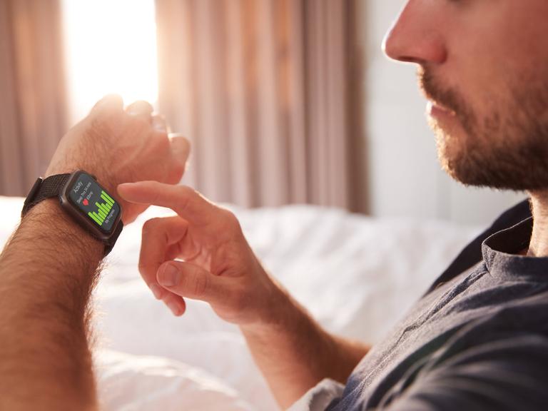 Ein Mann chekct den Verlauf seines Schlafs auf einem Fitnesstracker am Handgelenk.