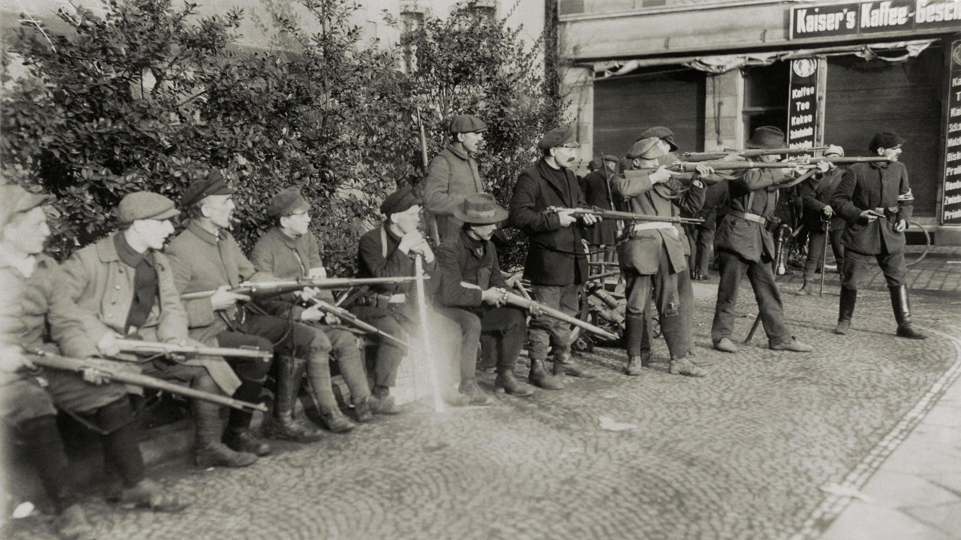 Schwarz-weißes Archivfoto: In einer Stadt im Ruhrgebiet 1920 stehen mehrere Männer nebeneinander. Sie haben alle Gewehre bei sich, einige davon schießen.