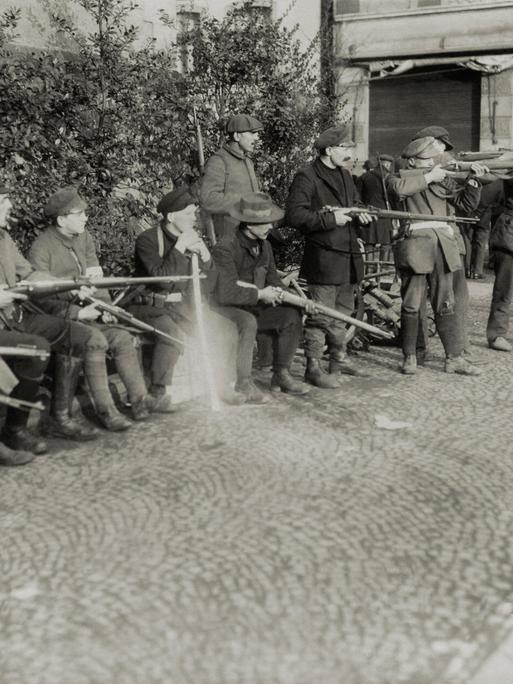 Schwarz-weißes Archivfoto: In einer Stadt im Ruhrgebiet 1920 stehen mehrere Männer nebeneinander. Sie haben alle Gewehre bei sich, einige davon schießen. Schwarz-weißes Archivfoto: In einer Stadt im Ruhrgebiet 1920 stehen mehrere Männer nebeneinander. Sie haben alle Gewehre bei sich, einige davon schießen.
