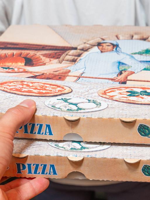 Eine Pizzalieferung an der Tür. Der uniformierte Lieferant gibt dem Empfänger zwei Pizzakartons.