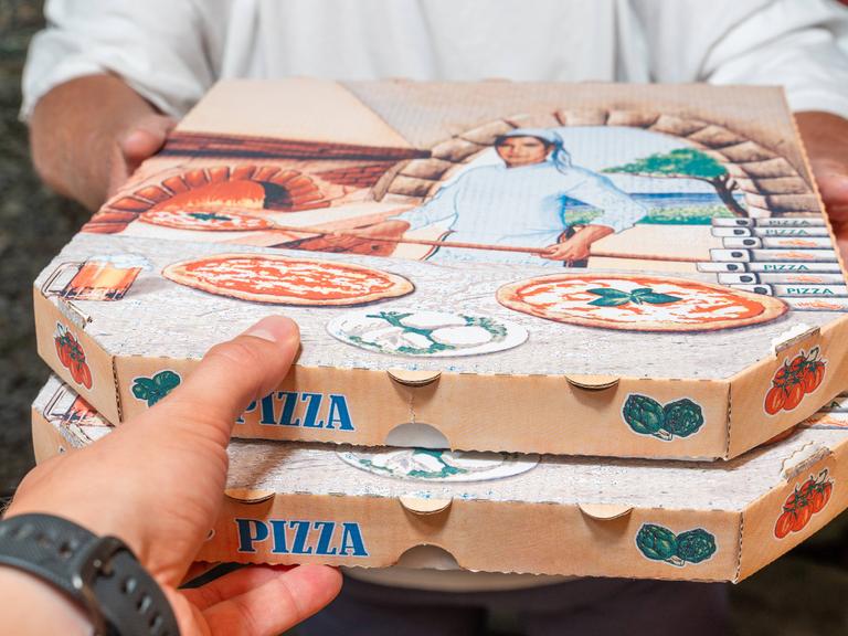 Eine Pizzalieferung an der Tür. Der uniformierte Lieferant gibt dem Empfänger zwei Pizzakartons.