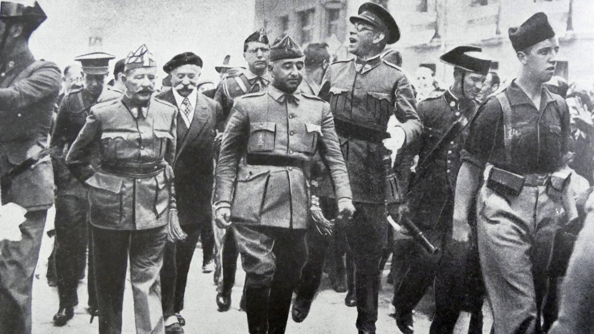 Schwarz-Weiß-Fotografie aus dem August 1936: General Francisco Franco schreitet in Burgos flankiert von den Generälen Emilio Mola, Miguel Cabanellas und José Cavalcanti durch eine Straße. Schwarz-Weiß-Fotografie aus dem August 1936: General Francisco Franco schreitet in Burgos flankiert von den Generälen Emilio Mola, Miguel Cabanellas und José Cavalcanti durch eine Straße.
