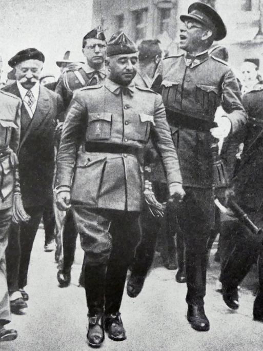 Schwarz-Weiß-Fotografie aus dem August 1936: General Francisco Franco schreitet in Burgos flankiert von den Generälen Emilio Mola, Miguel Cabanellas und José Cavalcanti durch eine Straße. Schwarz-Weiß-Fotografie aus dem August 1936: General Francisco Franco schreitet in Burgos flankiert von den Generälen Emilio Mola, Miguel Cabanellas und José Cavalcanti durch eine Straße.
