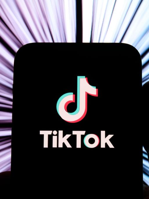 Illustration: TikTok-Logo auf einem schwarz gemalten Smartphone vor buntem Hintergrund