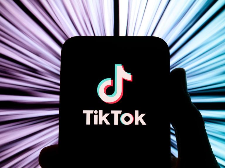 Illustration: TikTok-Logo auf einem schwarz gemalten Smartphone vor buntem Hintergrund