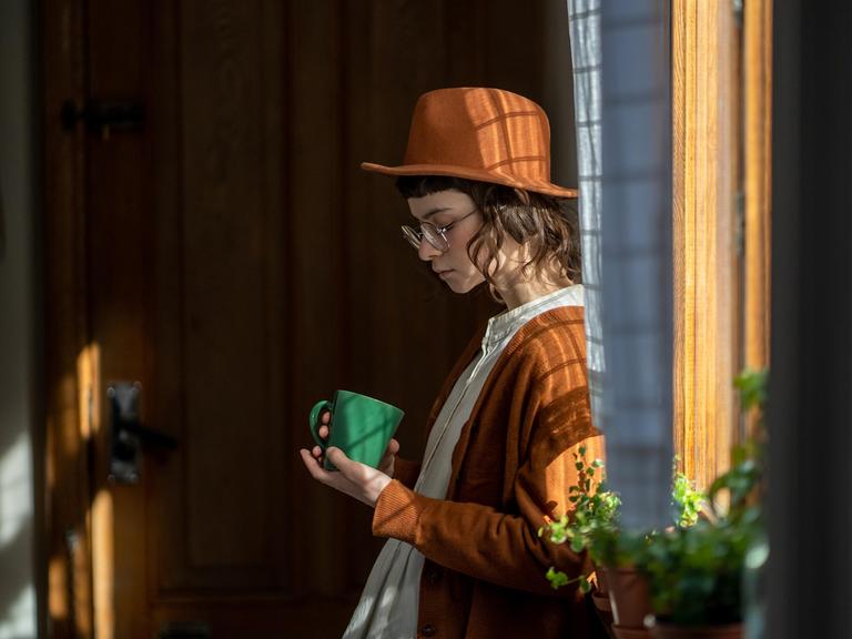 Eine Frau steht am Fenster und blickt traurig unten