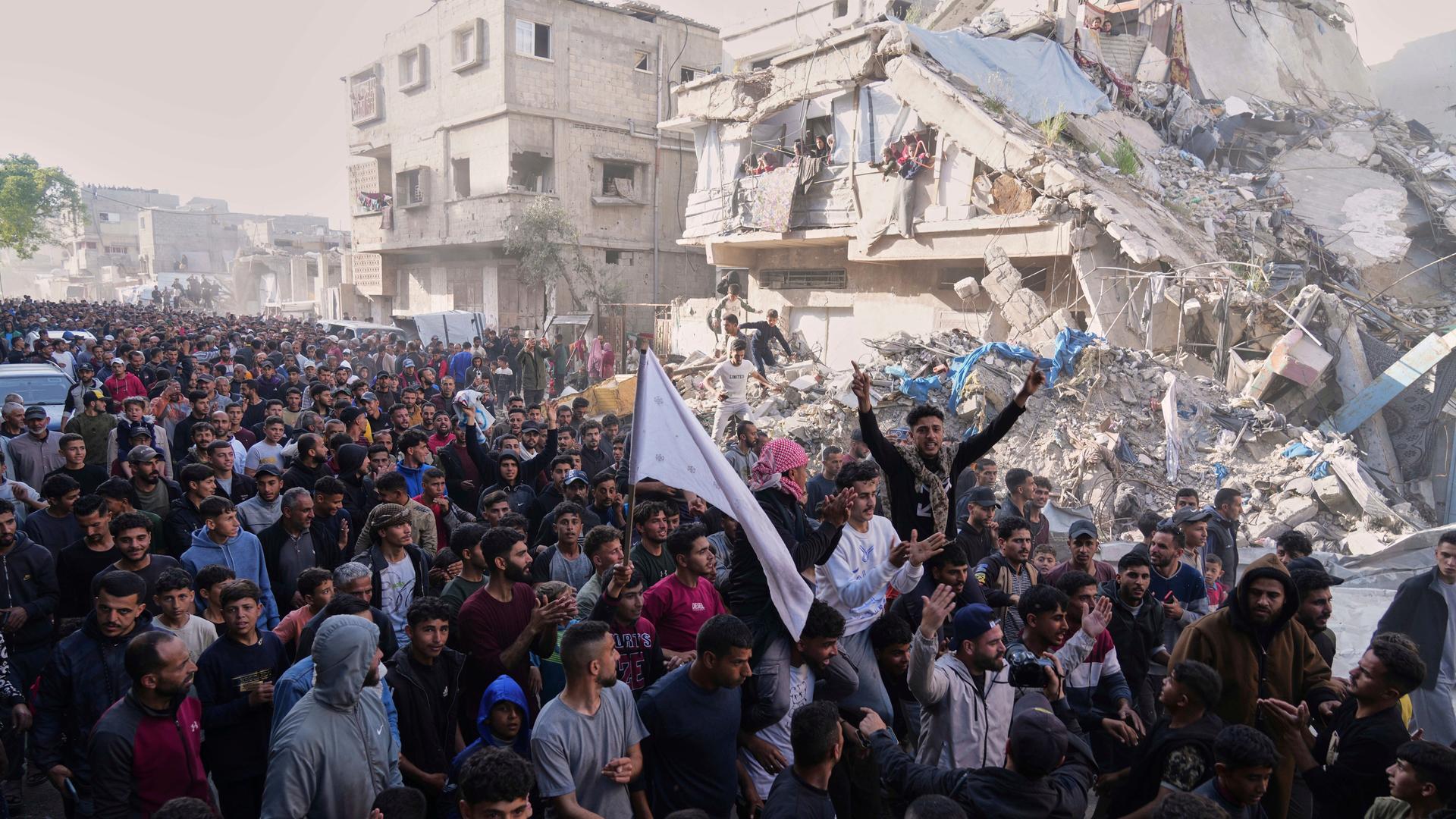 Palästinenser demonstrieren gegen Krieg und die regierende Hamas in Beit Lahiya im nördlichen Gazastreifen. Im Hintergrund ein zerstörtes Gebäude. (26.3.2025)