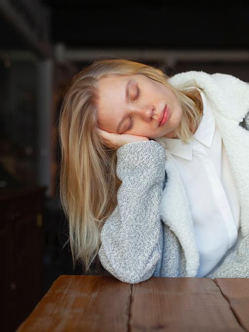 Foto einer jungen Frau, die den Kopf seitlich auf ihre Hand stützt und die Augen geschlossen hat Foto einer jungen Frau, die den Kopf seitlich auf ihre Hand stützt und die Augen geschlossen hat