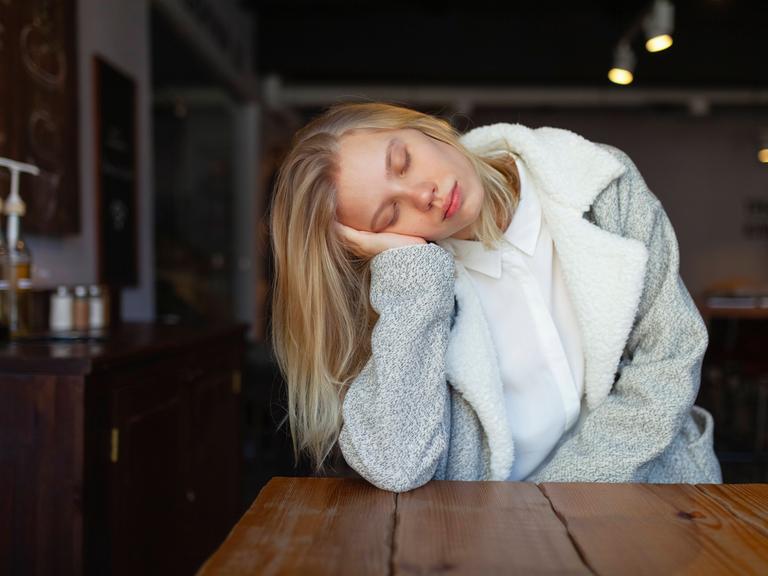 Foto einer jungen Frau, die den Kopf seitlich auf ihre Hand stützt und die Augen geschlossen hat Foto einer jungen Frau, die den Kopf seitlich auf ihre Hand stützt und die Augen geschlossen hat