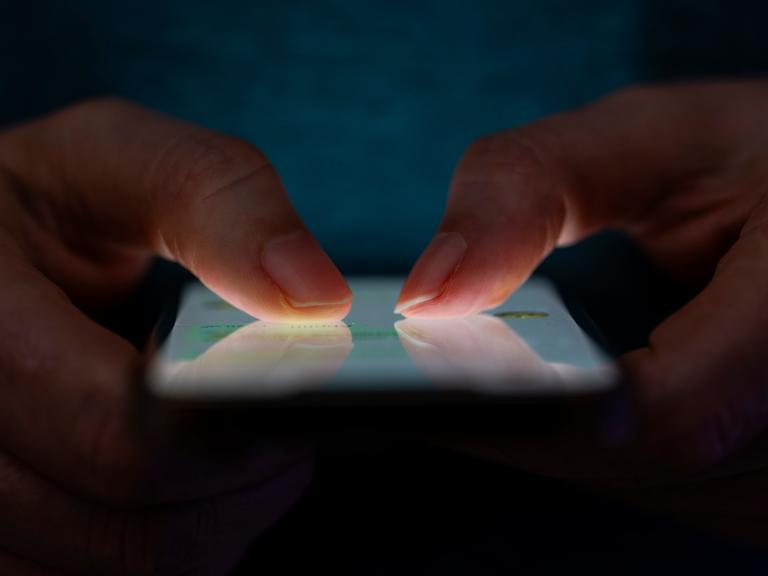 Ein Mensch hält ein Handy mit beiden Daumen auf dem Dsiplay