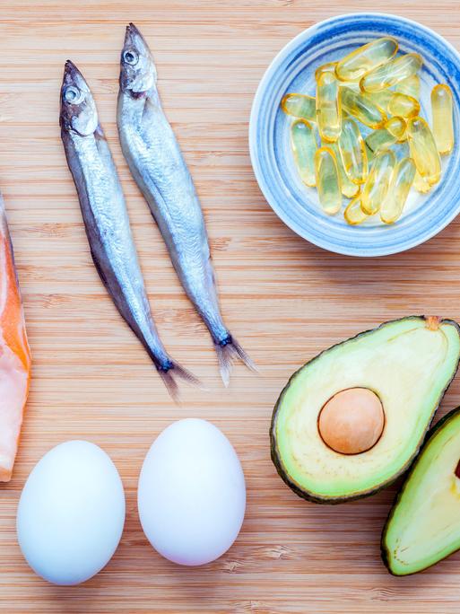 Lachs, Shishamo-Fisch, Fischöl, Avocado und Eier liegen auf einem Bambus-Schneidebrett