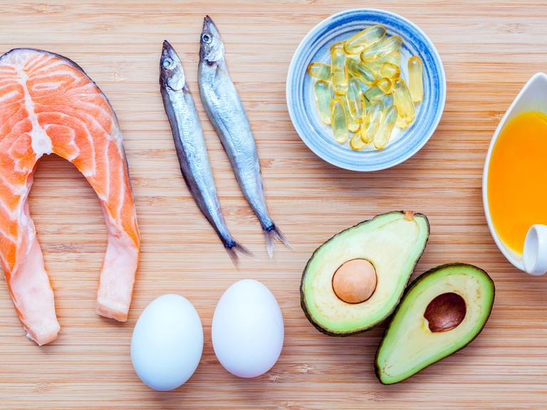 Lachs, Shishamo-Fisch, Fischöl, Avocado und Eier liegen auf einem Bambus-Schneidebrett