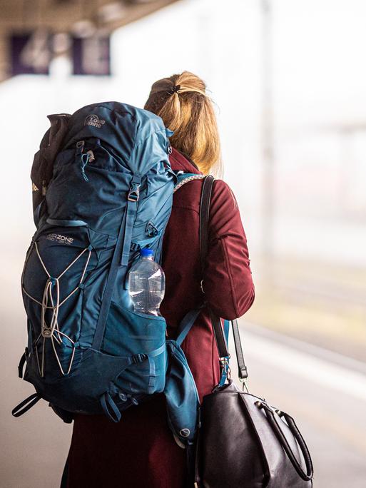 Eine Reisende steht am Morgen im Hauptbahnhof mit Rucksack. Eine Reisende steht am Morgen im Hauptbahnhof mit Rucksack.