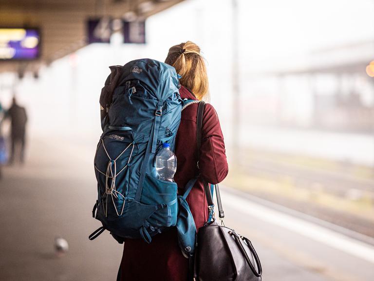 Eine Reisende steht am Morgen im Hauptbahnhof mit Rucksack. Eine Reisende steht am Morgen im Hauptbahnhof mit Rucksack.