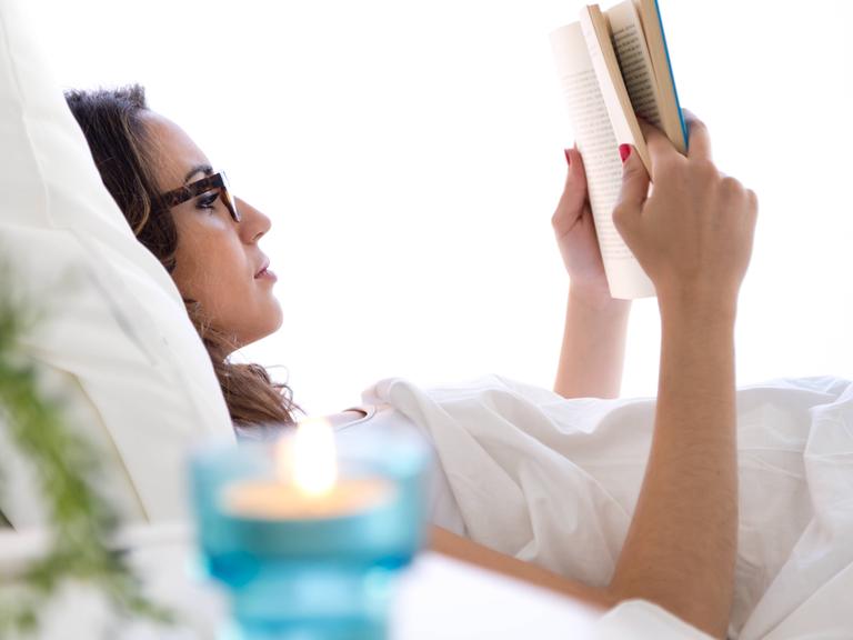 Eine Frau liegt im Bett und liest ein Buch