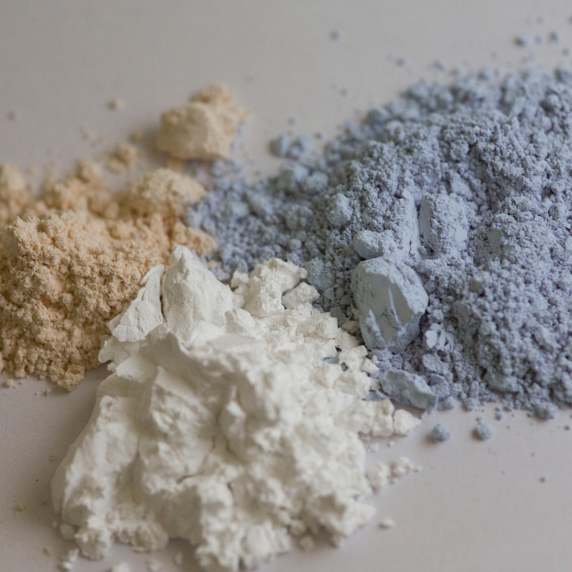 Auf einem Tisch liegen drei Pulverhaufen in braun, weiß und blau. Es sind die Seltenen Erden Ceroxid, Yttriumoxid und Neodymoxid.