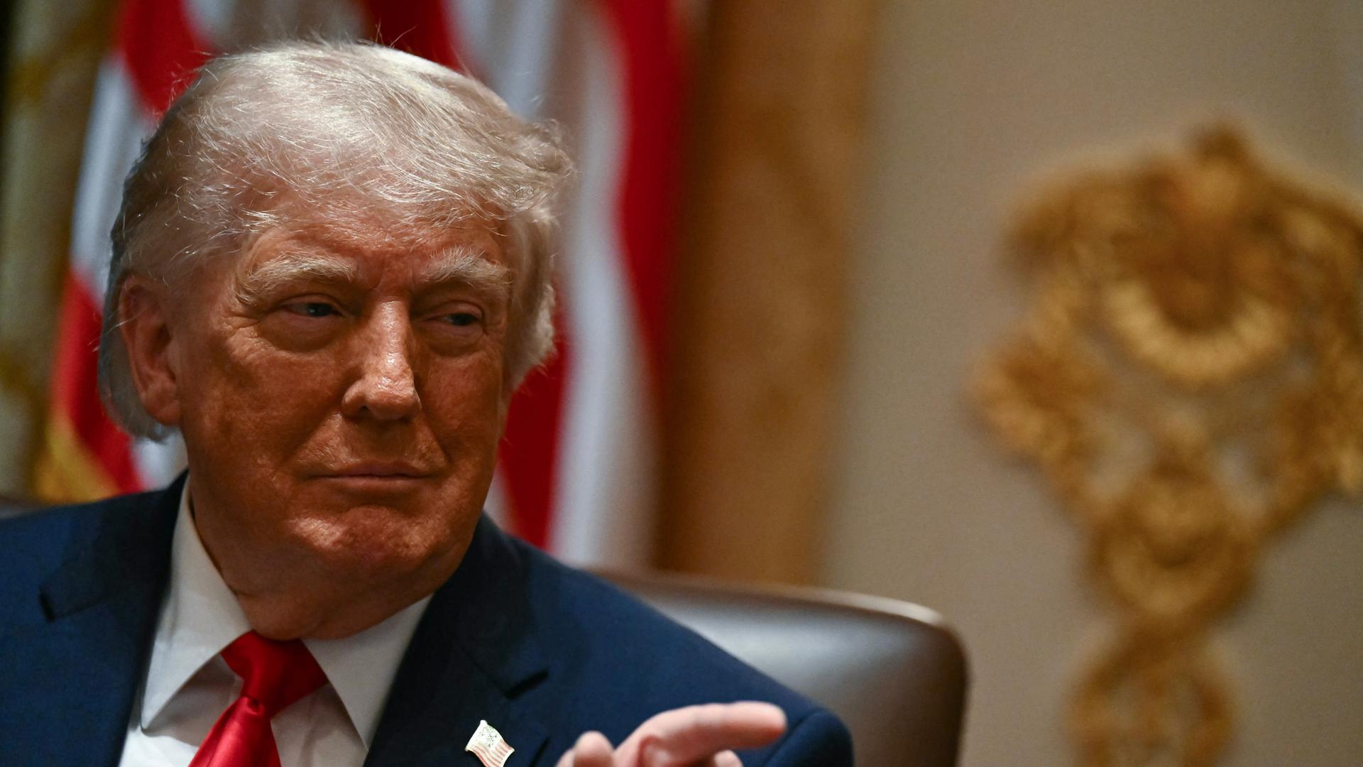 Portrait von Donald Trump vor einer US-Flagge, er zeigt mit dem Finger nach rechts Portrait von Donald Trump vor einer US-Flagge, er zeigt mit dem Finger nach rechts