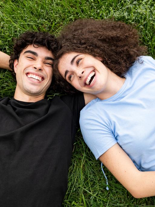 Ein junges Paar liegt im Gras und lacht