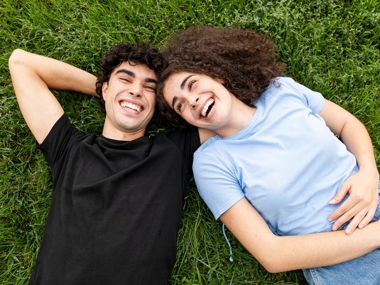 Ein junges Paar liegt im Gras und lacht