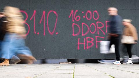 An einer Baustellen-Holzverkleidung in Düsseldorf ist mit rosaroter Farbe der Schriftzug „31.10. 16:00 DDORF HFB“ gesprayt.