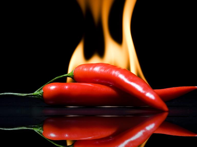 Zwei Peperonis vor Flammen im Hintergrund