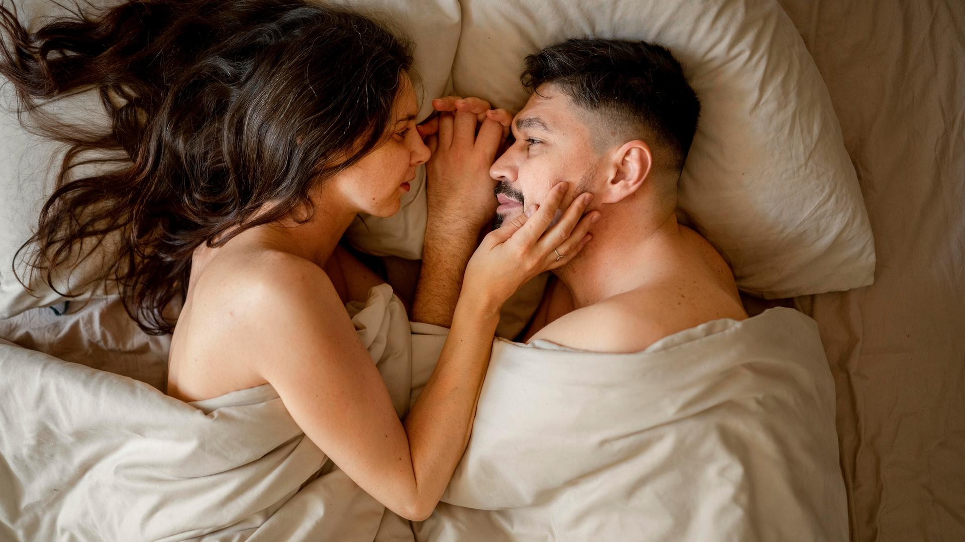 Eine Frau und ein Mann liegen im Bett, schauen sich an und berühren sich mit den Händen zärtlich. Eine Frau und ein Mann liegen im Bett, schauen sich an und berühren sich mit den Händen zärtlich.
