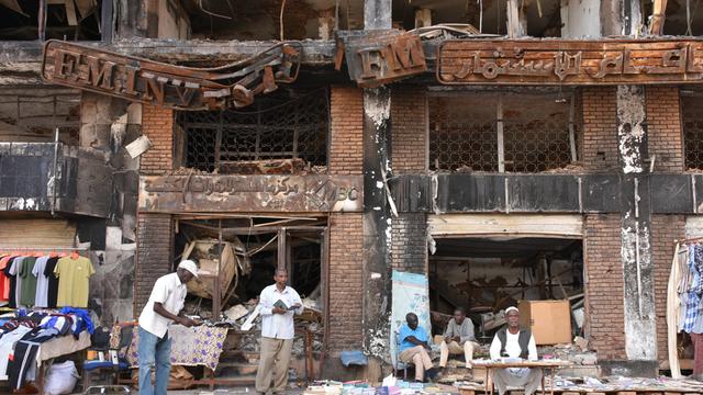 In der sudanesischen Hauptstadt Khartum herrscht auf der Straße wieder Alltag: Händler verkaufen Kleidung und Bücher, hinter ihnen steht ein Gebäude mit schwer beschädigter Fassade.
