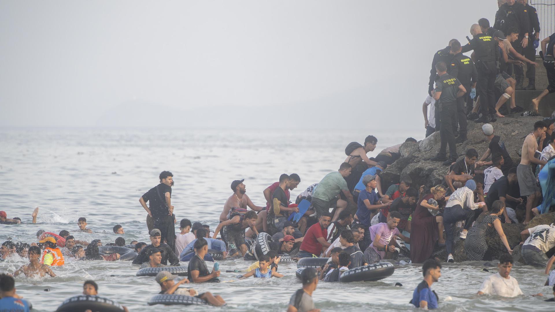 Menschen schwimmen im Meer und klettern auf einen Felsen, auch Sicherheitskräfte sind vor Ort Menschen schwimmen im Meer und klettern auf einen Felsen, auch Sicherheitskräfte sind vor Ort