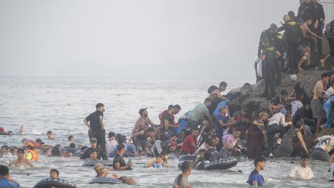 Menschen schwimmen im Meer und klettern auf einen Felsen, auch Sicherheitskräfte sind vor Ort