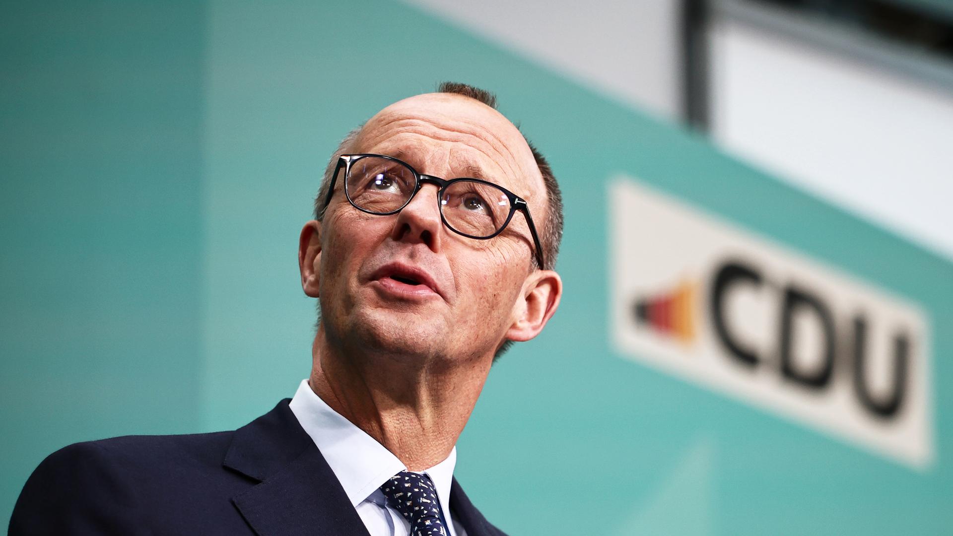  Merz spricht während einer Pressekonferenz. im Hintergrund eine grüne Wand mit dem CDU-Logo. Merz ist schräg von unten fotografiert.