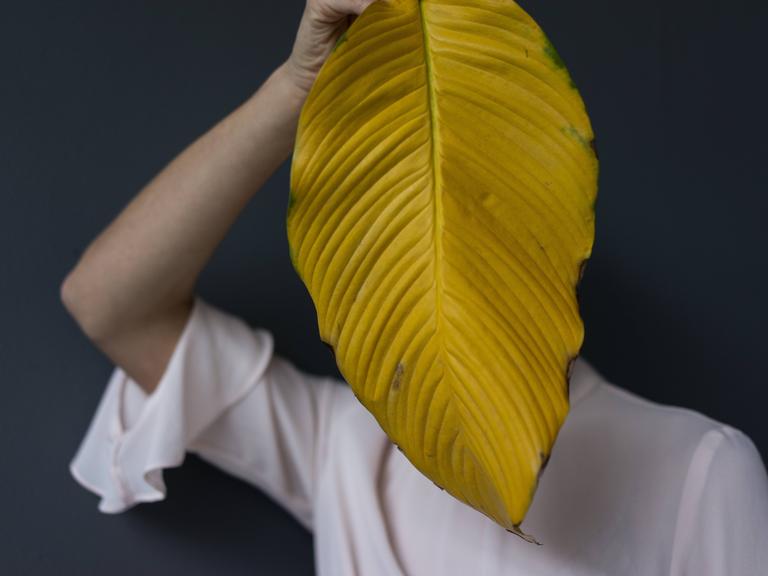 Eine Frau verbirgt sich hinter einem Blatt Eine Frau verbirgt sich hinter einem Blatt