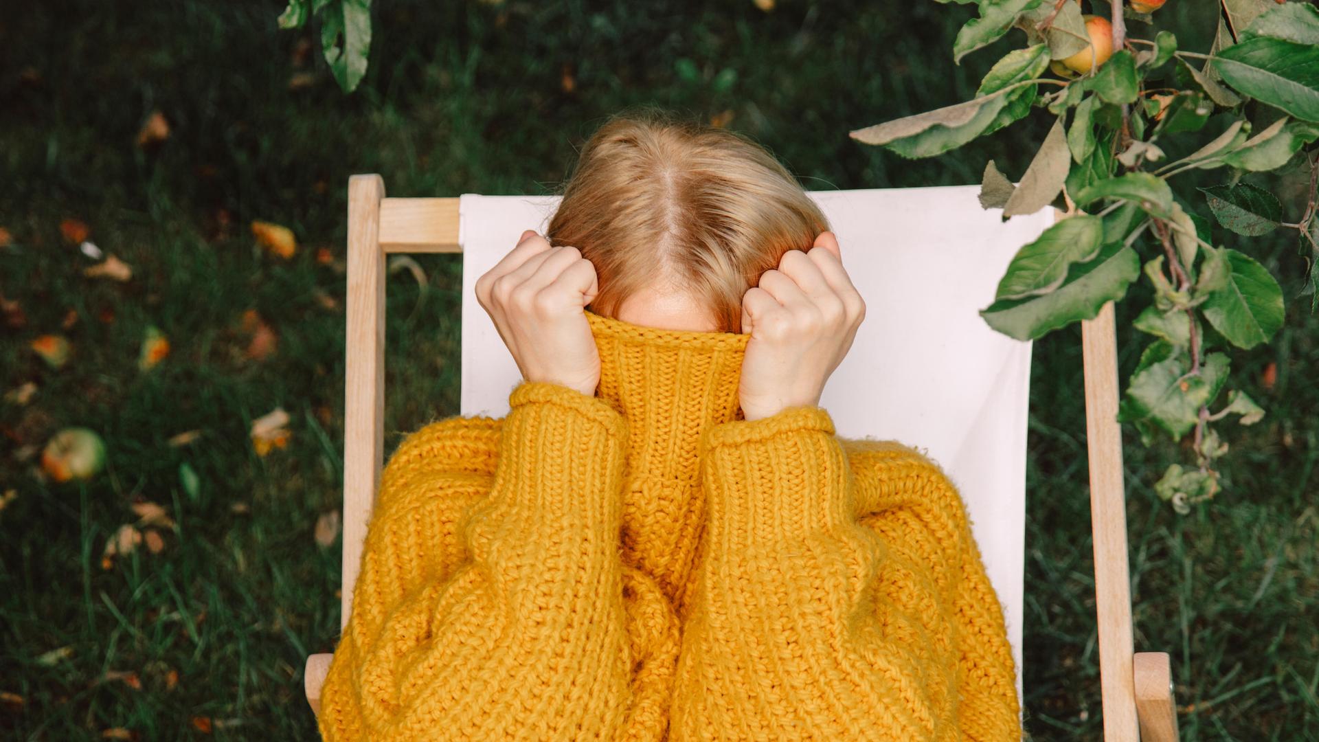 Eine Frau versteckt ihr Gesicht hinter ihrem Pullover Eine Frau versteckt ihr Gesicht hinter ihrem Pullover