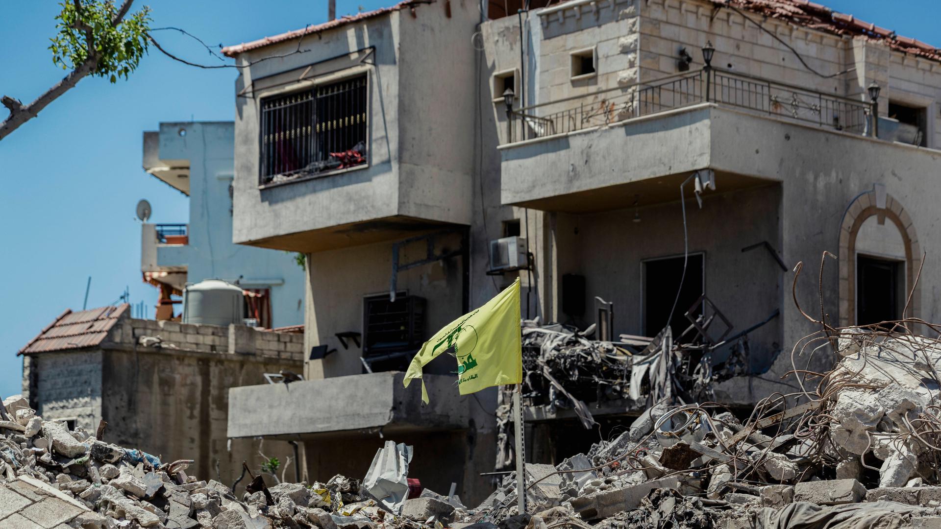 Eine zerrissene Hisbollah-Flagge steht inmitten der Ruinen zerstörter Wohngebäude. Eine zerrissene Hisbollah-Flagge steht inmitten der Ruinen zerstörter Wohngebäude.